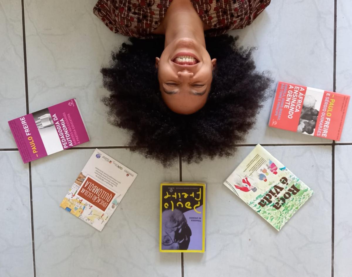 Gabriele Miranda, no chão, cercada de livros de Paulo Freire e do livro Roça É Vida