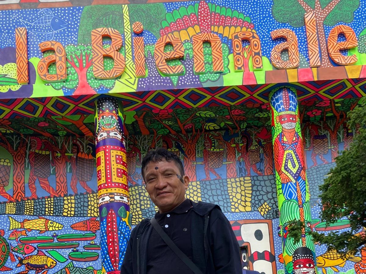 At the entrance to the Biennale, Joseca Yanomami poses in front of a seven hundred square meter mural painted by the Huni Kuin Artists Movement (MAHKU), an indigenous artistic collective from the Amazon | Daniel Jabra