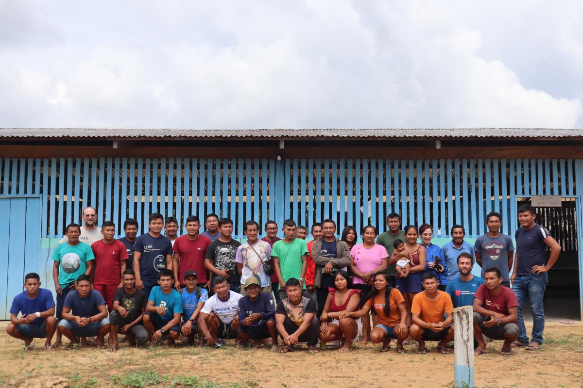 Aproximadamente 40 pessoas que participaram da oficina posam para foto na frente de uma casa de madeira azul. 