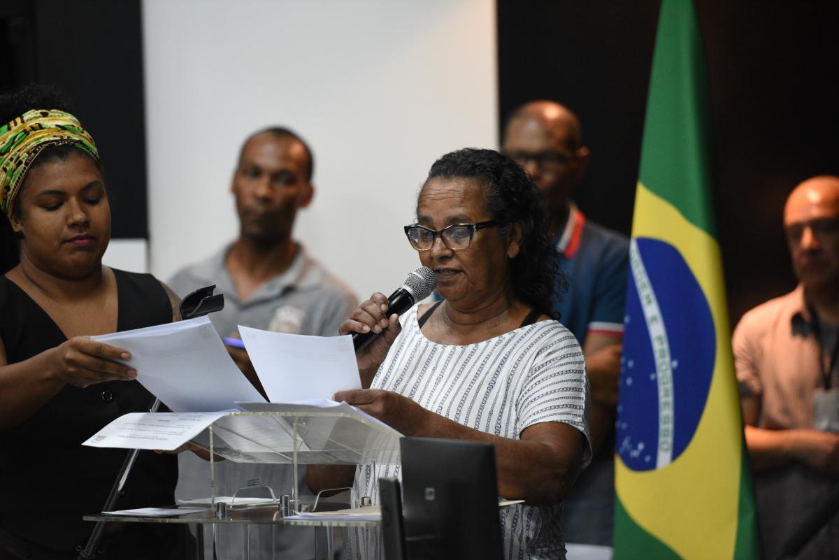 Edna Aparecida faz a leitura da carta das Comunidades Quilombolas ao microfone. Atrás dela, tem uma bandeira do Brasil posicionada e também algumas lideranças quilombolas