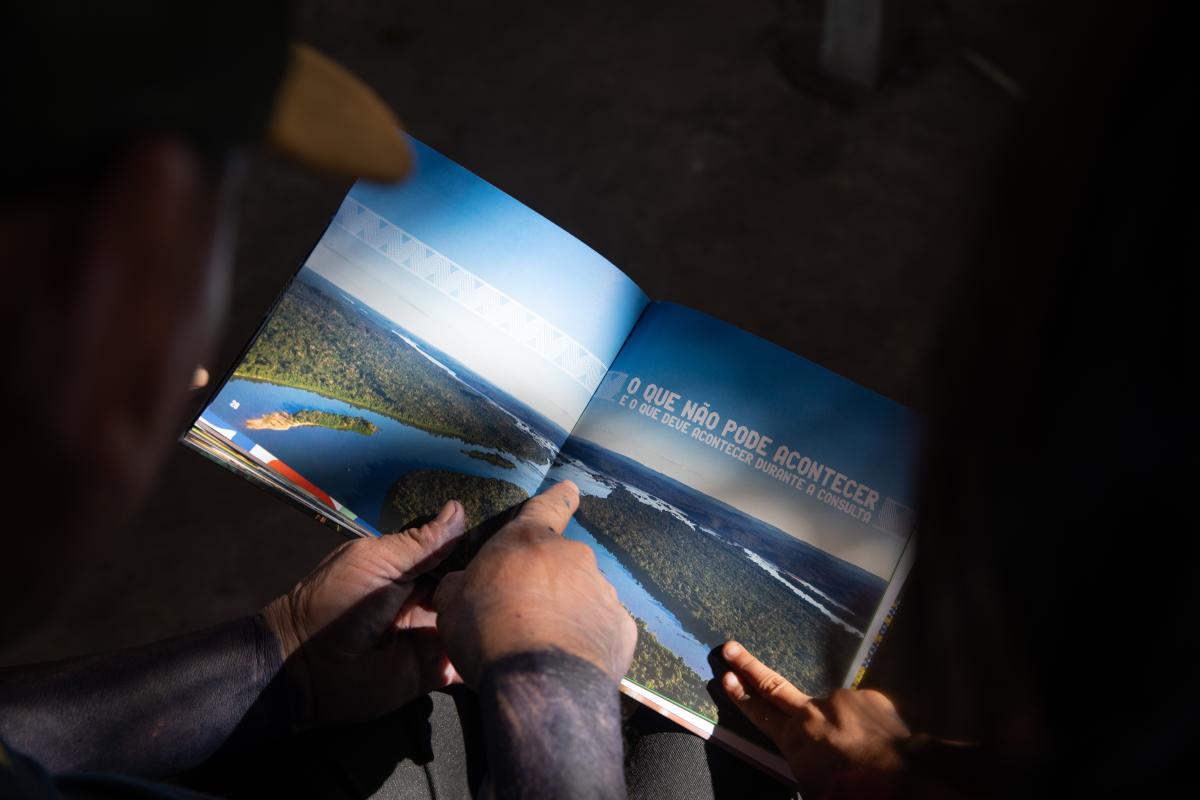 Foto mostra Protocolo de Consulta Parakanã na mão de um indígena. Ele aponta para o livro